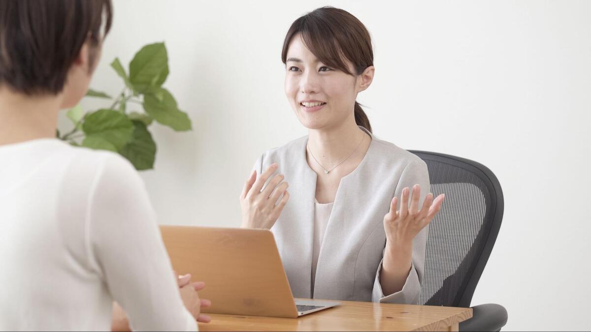 デスクでノートパソコンを前に、身振り手振りを交えて話す女性