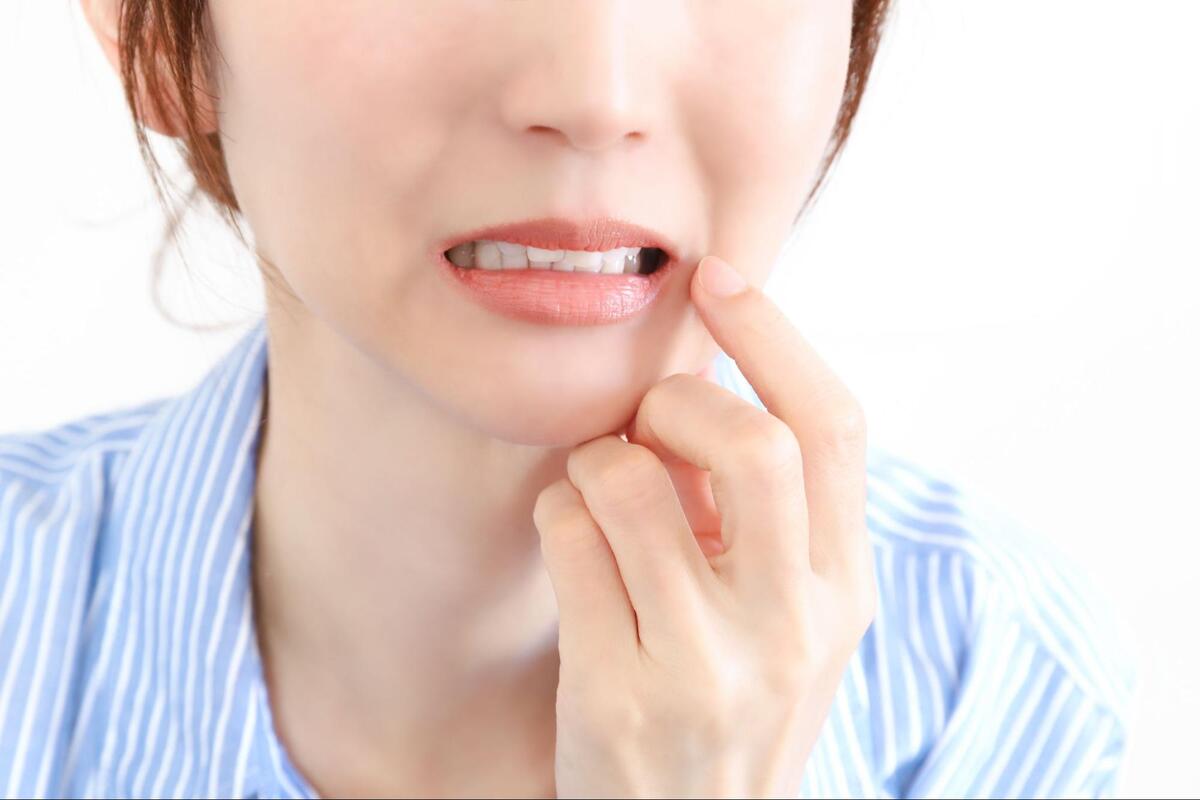 歯の痛みや口元の違和感を訴えるように、人差し指で頬を指さす女性のクローズアップ