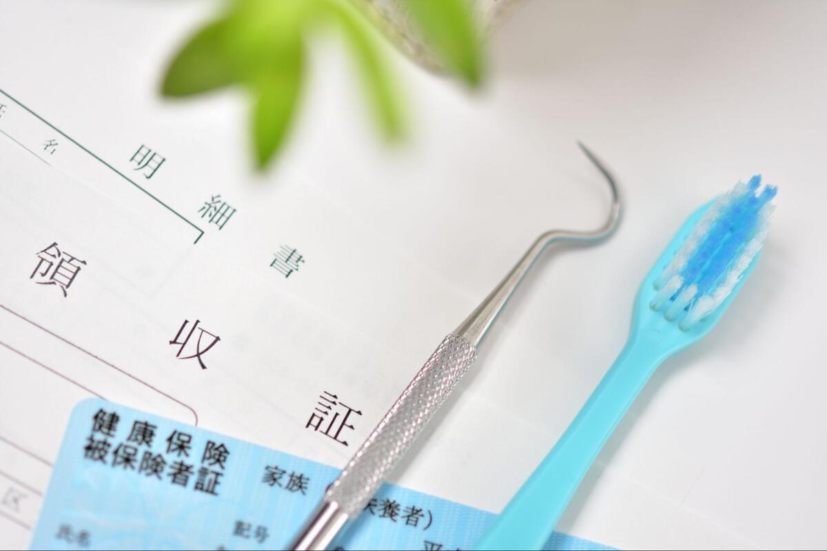 歯科の領収明細書や健康保険証の上に置かれた、診療用の探針と水色の歯ブラシ