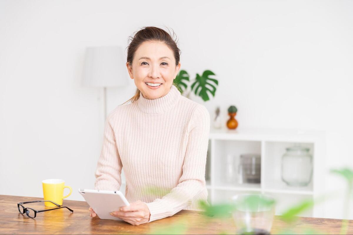木製テーブルでタブレットを手に持ち笑顔で座るシニア女性