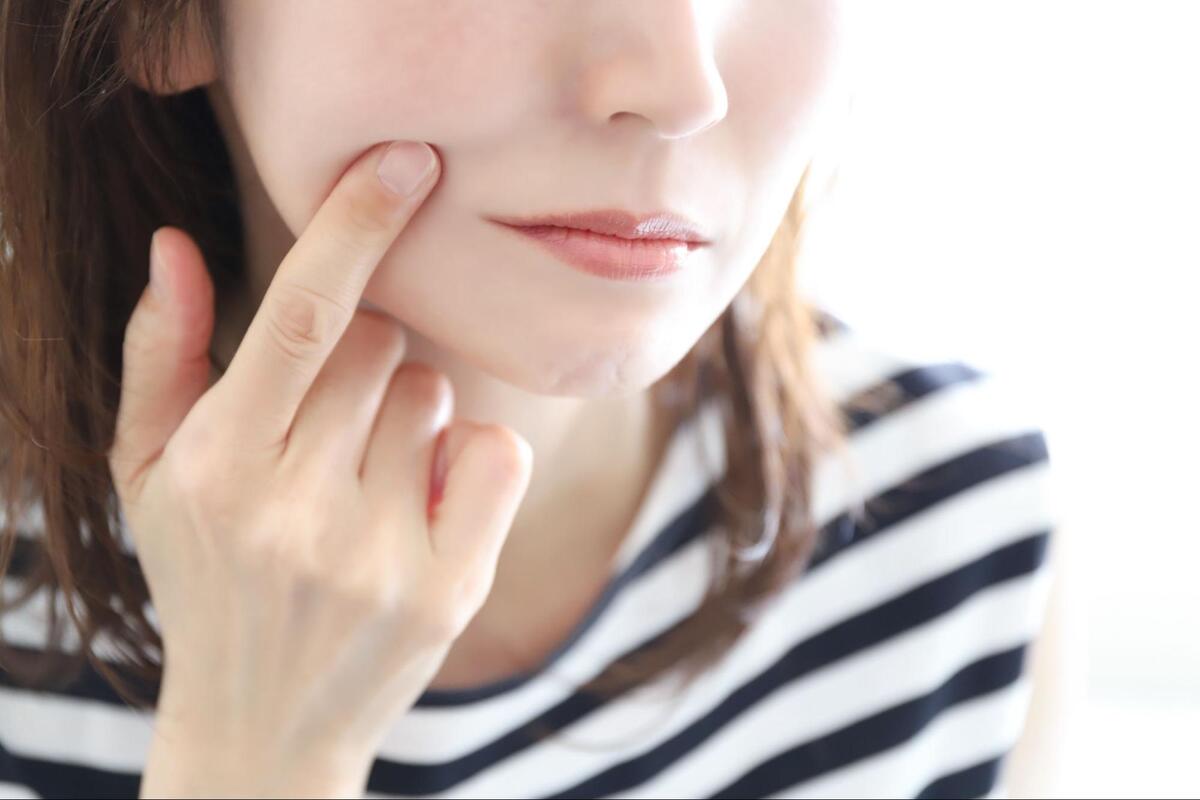 歯痛や口元の違和感を訴えるように、人差し指で自分の右側の頬に触れている女性の口元のアップ