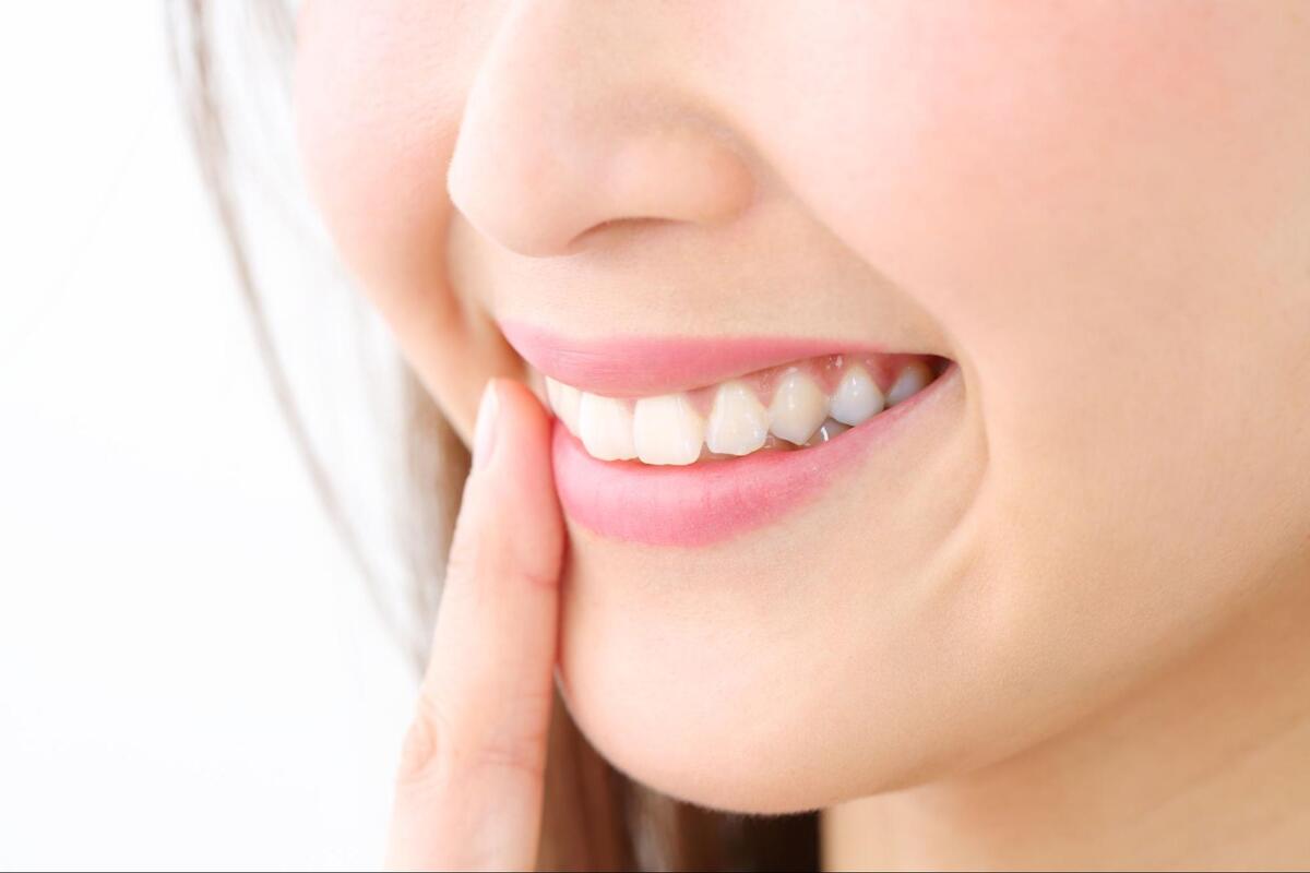 人差し指を口元に添えて、健康的できれいな白い歯とピンク色の歯茎を見せて微笑む女性のアップ