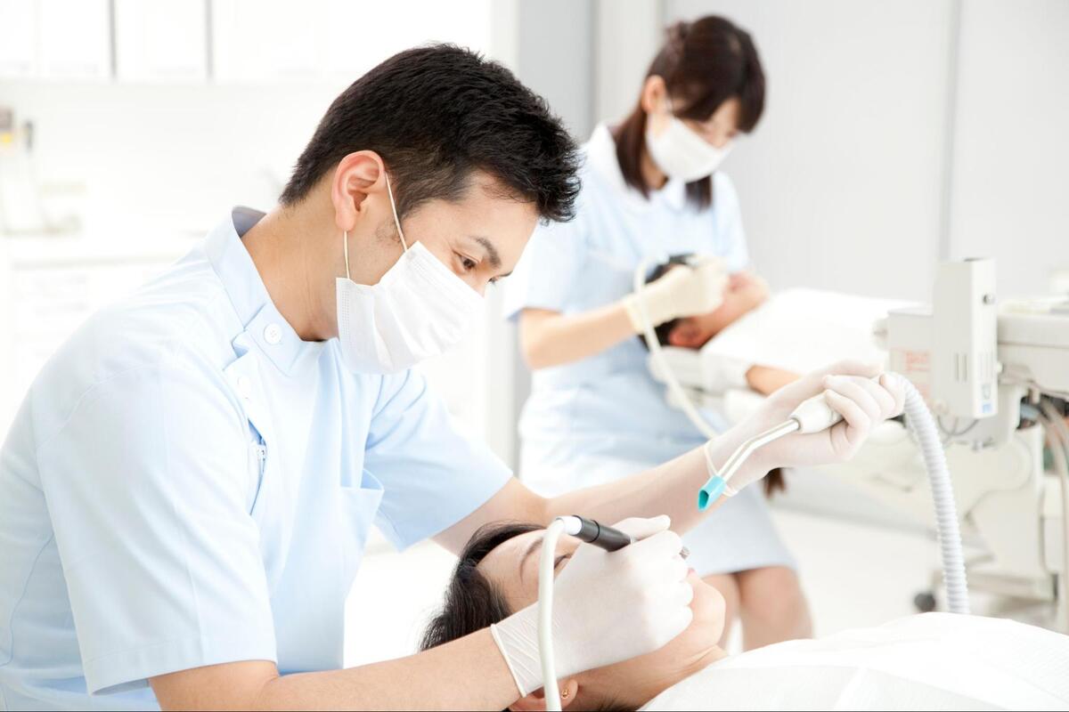 歯科診療室にて、マスクと手袋を着用した歯科医師が横たわる患者の口内を治療している様子
