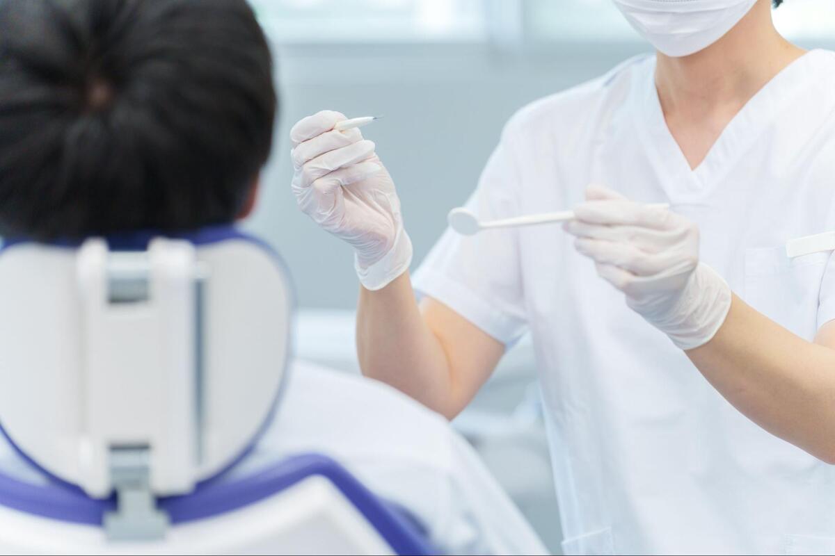 歯科診療室で、マスクと手袋を着用した歯科医師が口腔鏡と探針で患者の歯を検査している様子